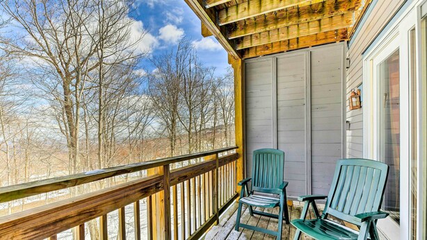 A wooden deck with two green Adirondack chairs, a wooden railing, and a view of leafless trees. - Inviting Ski-in/ski-out Condo at Jay Peak Resort! (North Troy)
