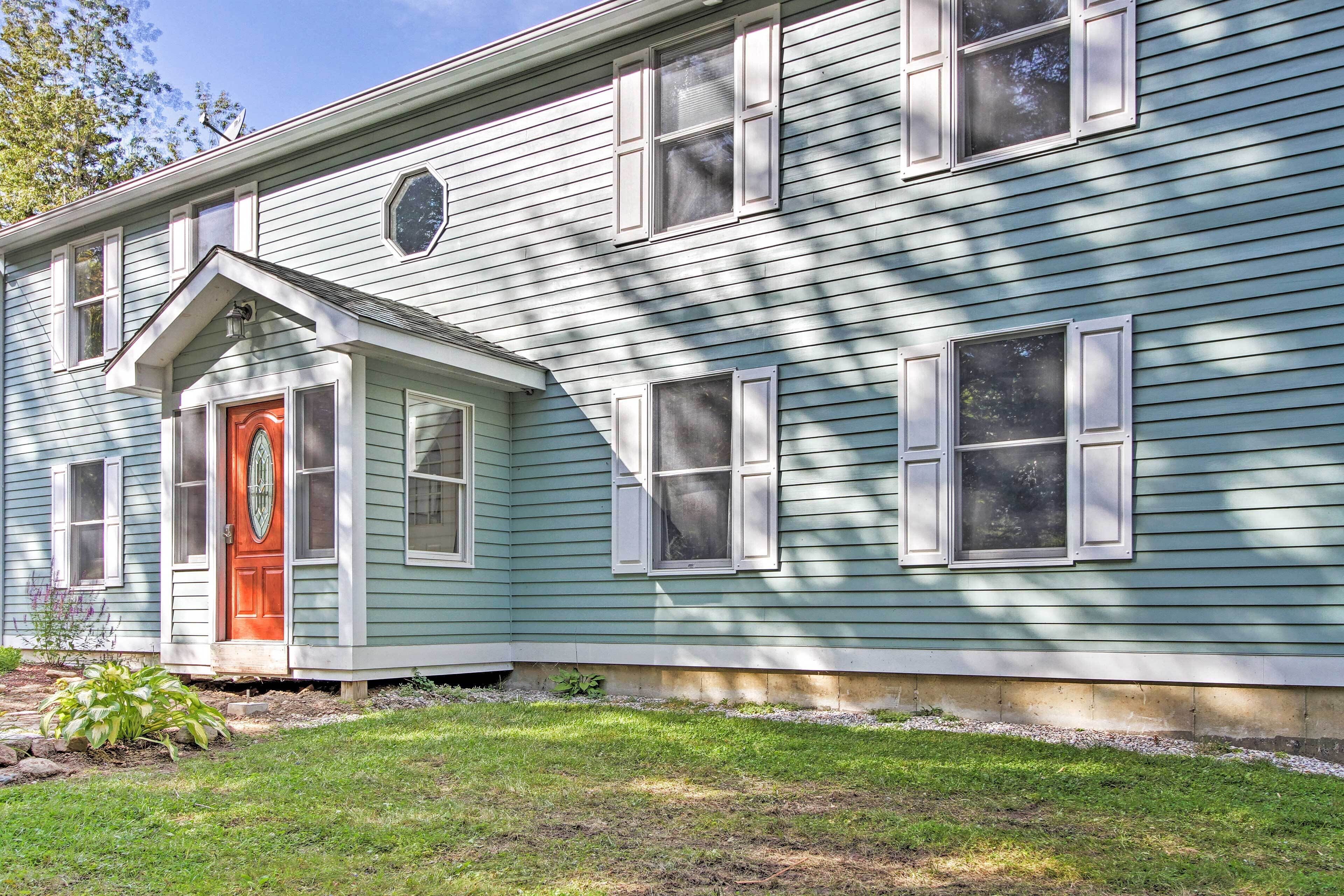 A two-story house with a red door and white shutters, featuring a small front porch and a well-maintained lawn.