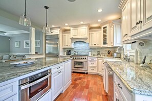 A modern kitchen with white cabinetry, granite countertops, stainless steel appliances, and a stone backsplash.