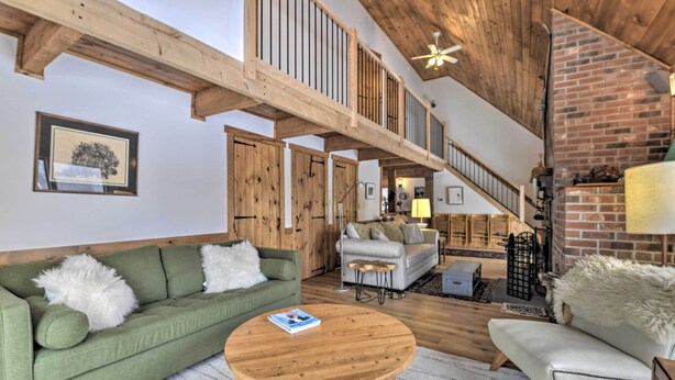A spacious living area with a green sofa, a round wooden coffee table, and a white armchair. A staircase leads to an upper level with a wooden railing.