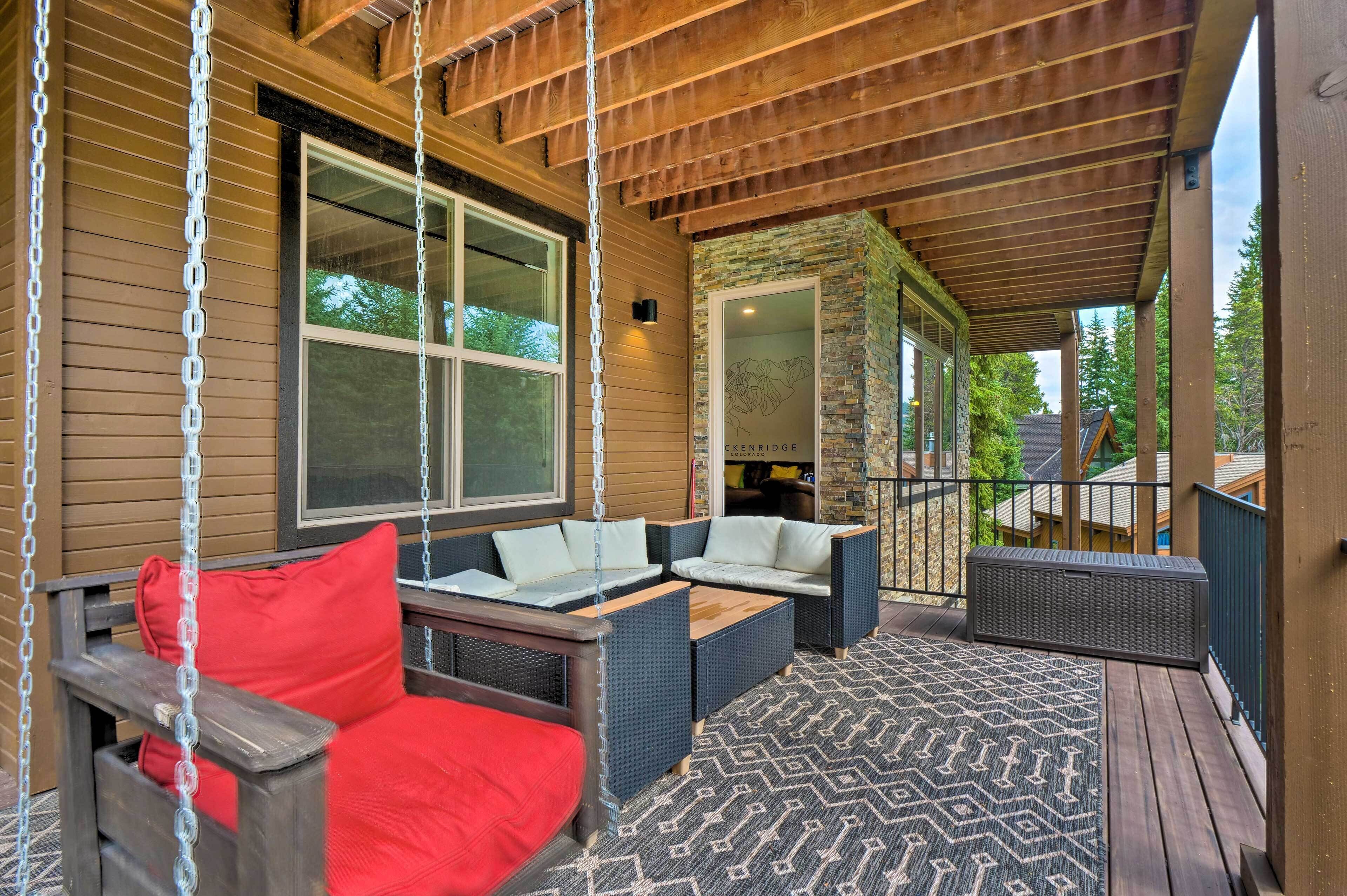 A covered porch with wicker furniture, a swing, and a view of a house with a stone facade.
