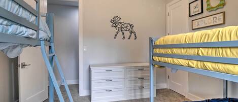 A bedroom with bunk beds, a white dresser, and wall decorations including a moose and framed items.