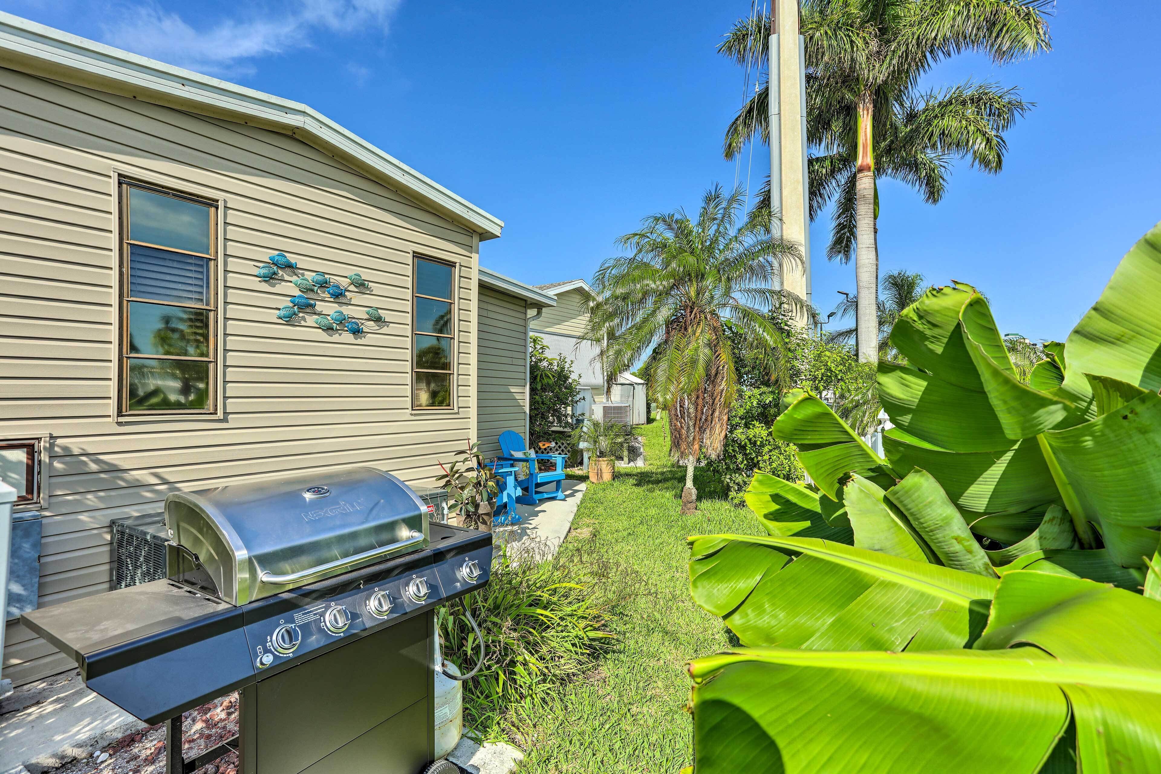 Une maison avec un barbecue dans le jardin, entourée d’une végétation luxuriante et de palmiers.