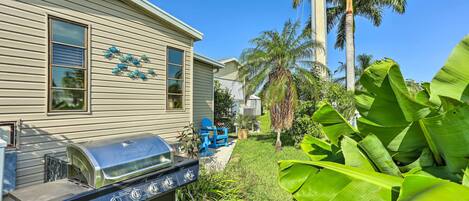A house with a barbecue grill in the backyard, surrounded by lush greenery and palm trees.