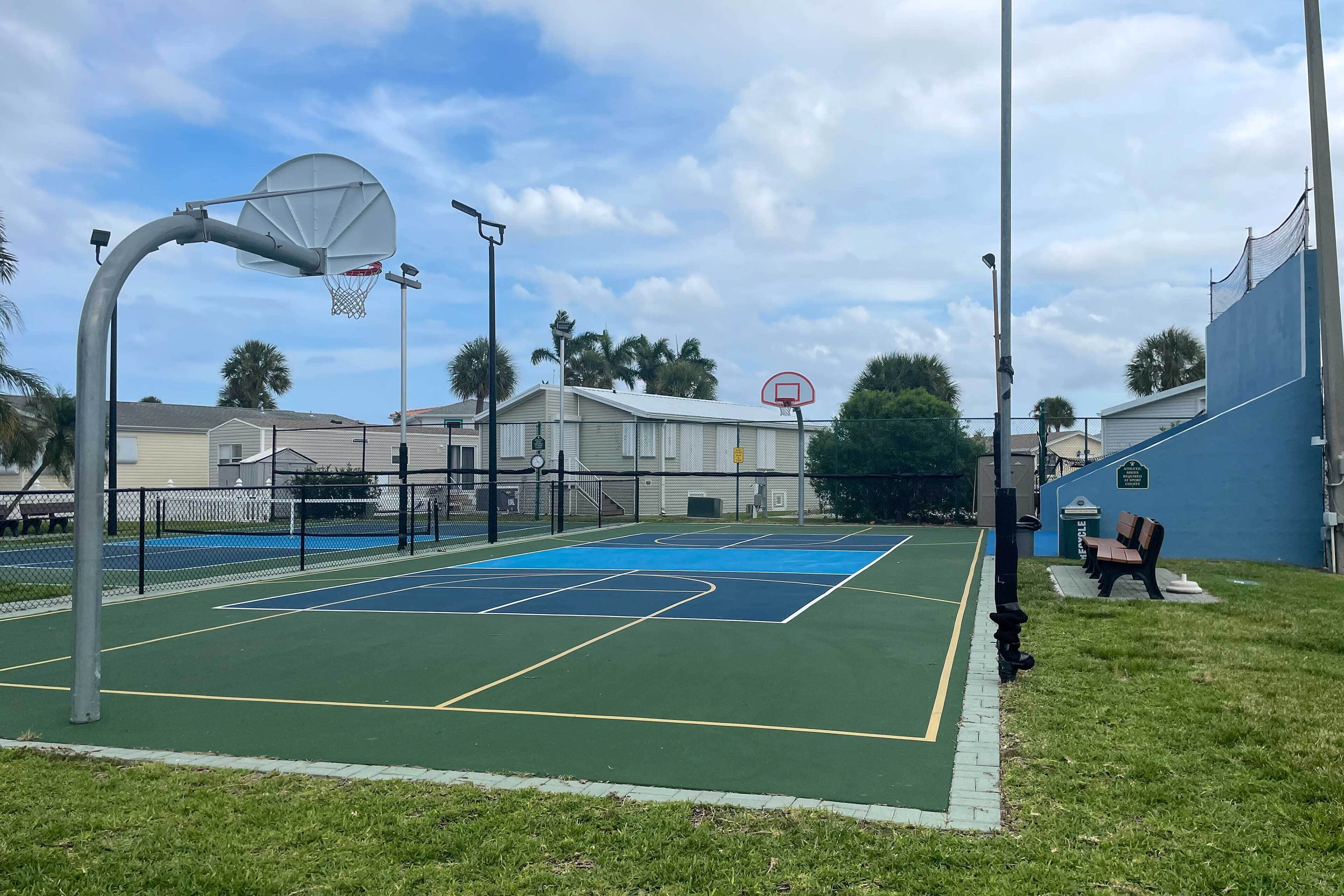 Ein Basketballplatz im Freien mit Netz, Zaun und Bank.
