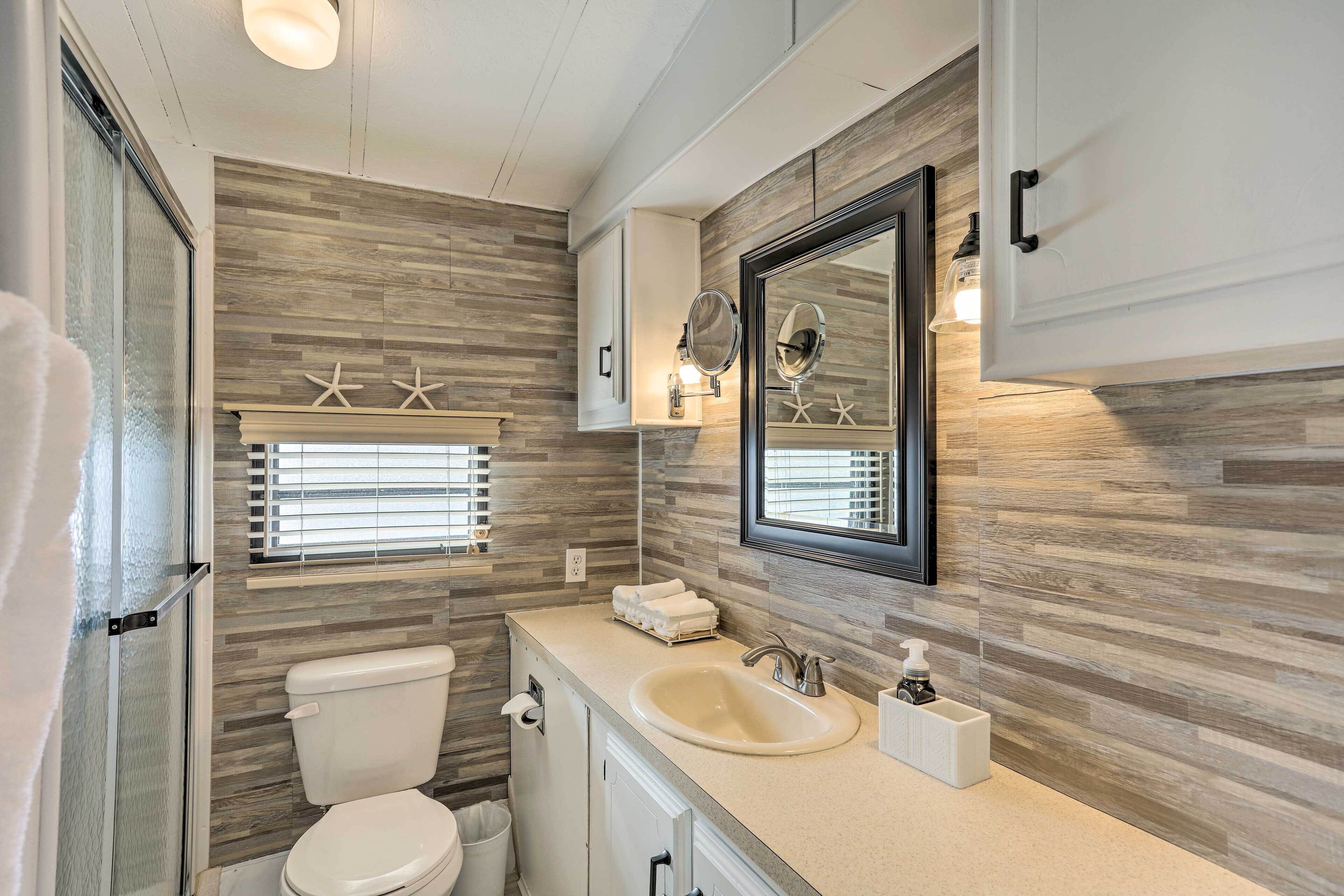A modern bathroom with a wooden wall backsplash, a large mirror, a toilet, and a sink with a soap dispenser.