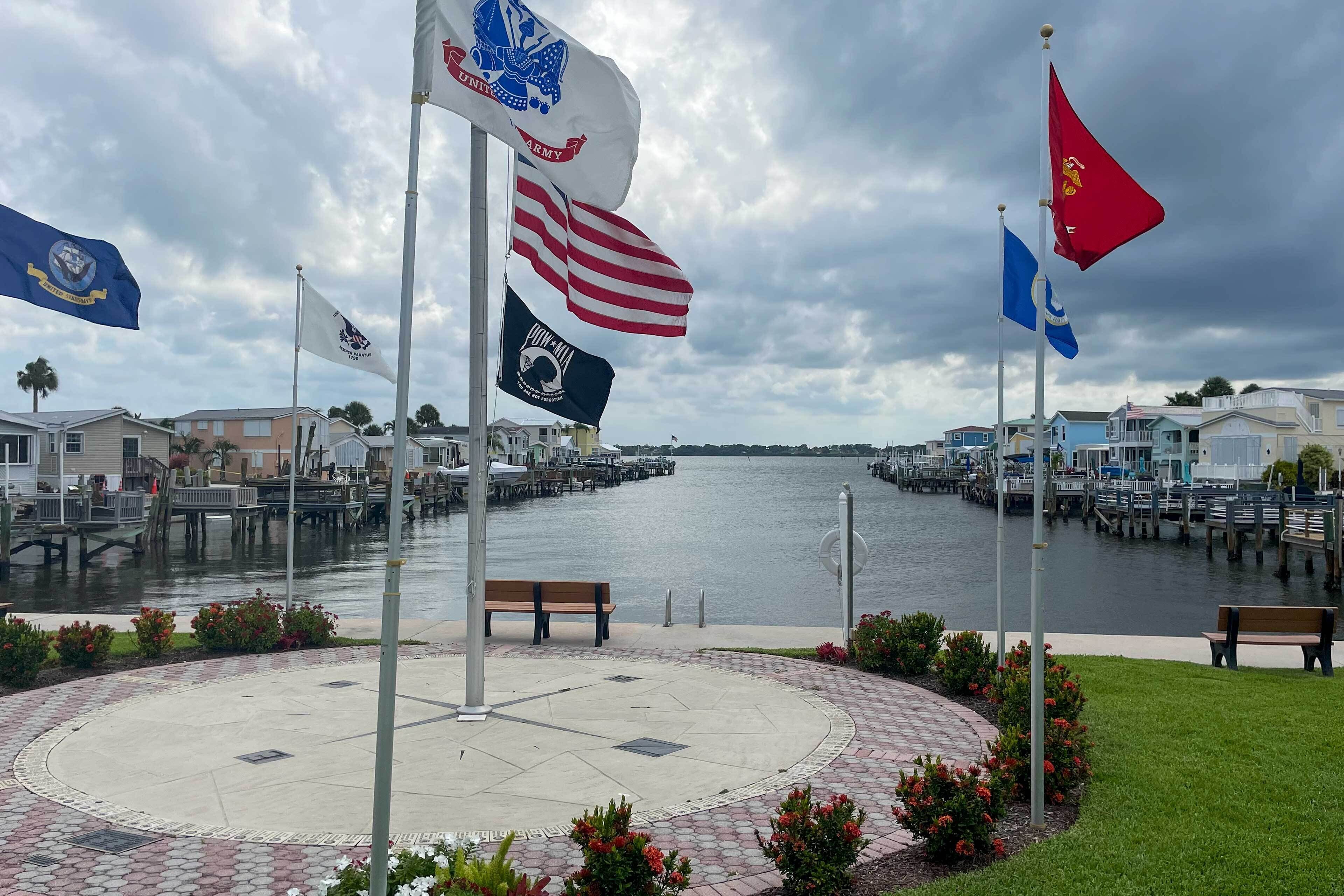 A waterfront promenade with a circular brick walkway, benches, and flags.