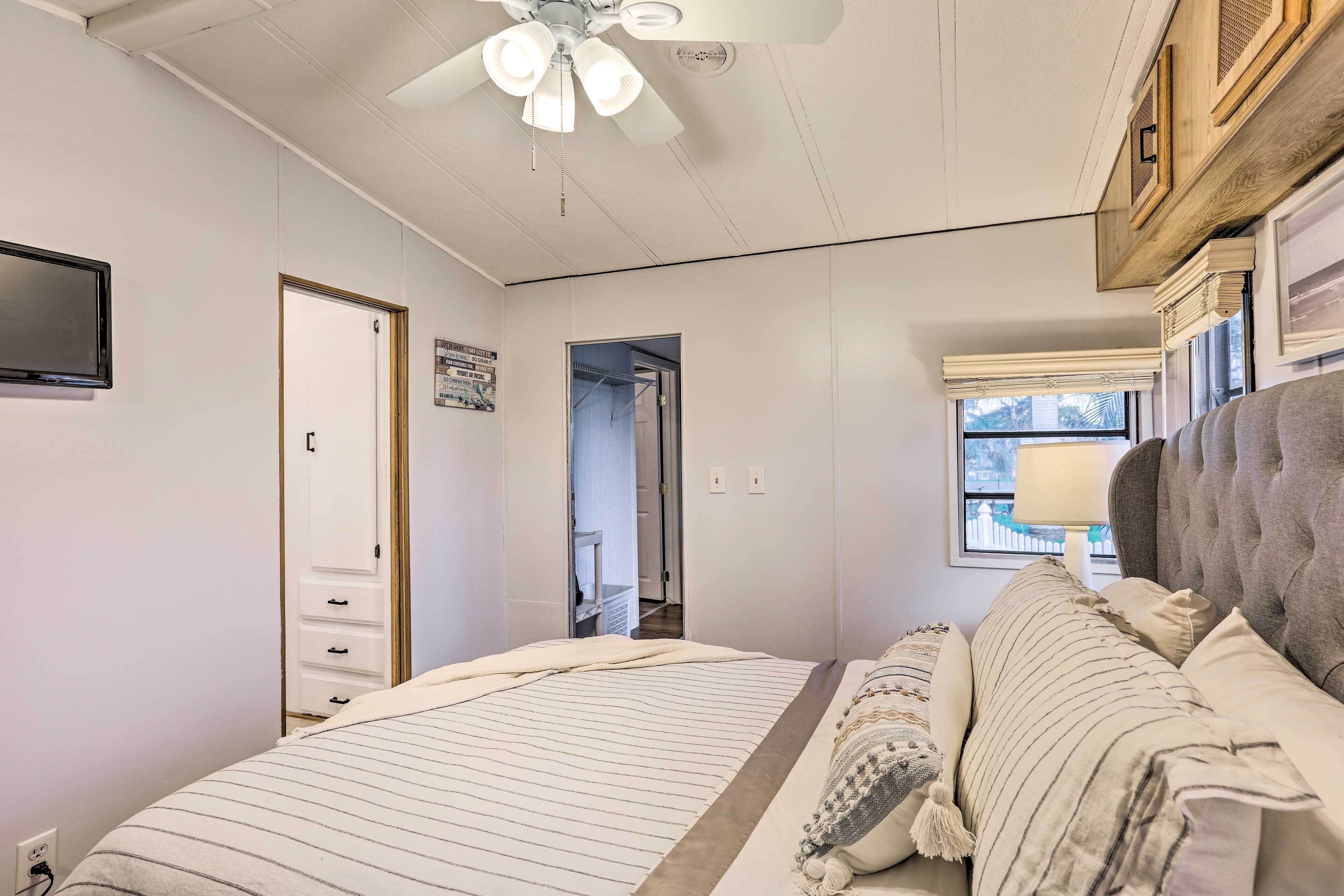 Ein Schlafzimmer mit einem Bett, einem Deckenventilator, einem Fenster mit Aussicht und einer Tür zu einem anderen Raum.