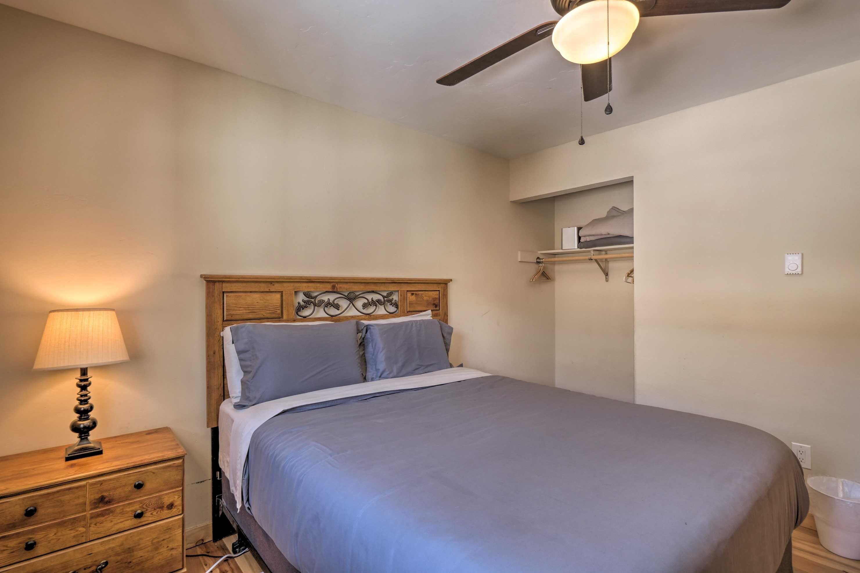 Un dormitorio con cama, mesita de noche de madera, lámpara, ventilador de techo y estanterías empotradas.