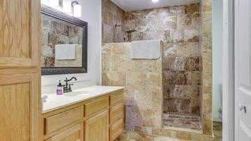 A bathroom with a wooden vanity, a large mirror, a shower with a glass door, and a tiled floor.
