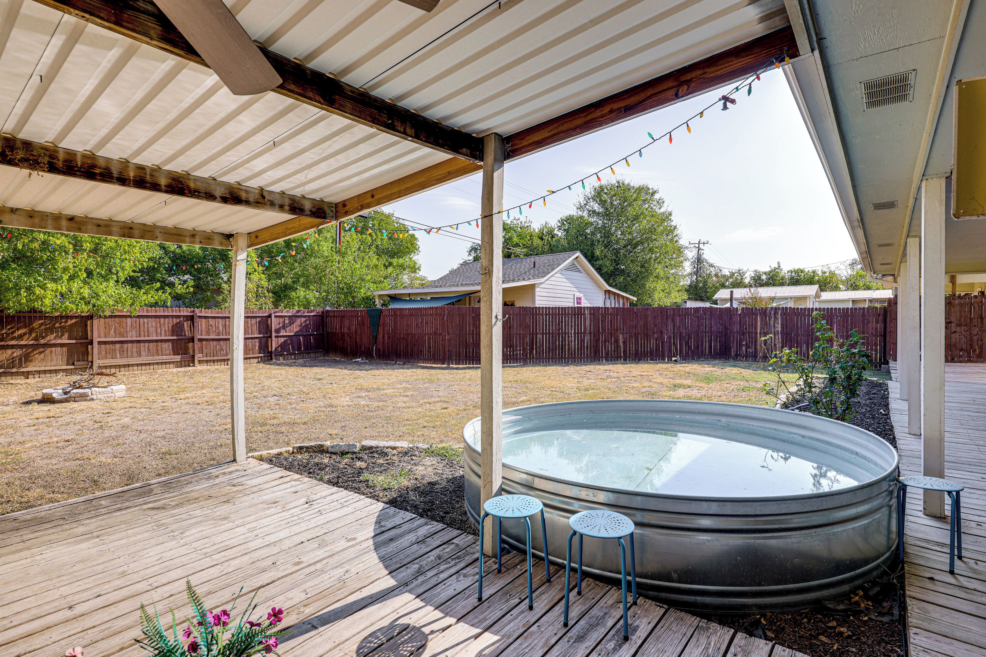 A covered outdoor area with a hot tub, wooden deck, and two stools.