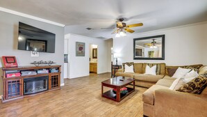 A living room with a fireplace, a ceiling fan, a large TV, and a sofa. - Charming Lake Retreat w/ Patio & Boat Parking! (Canyon Lake)
