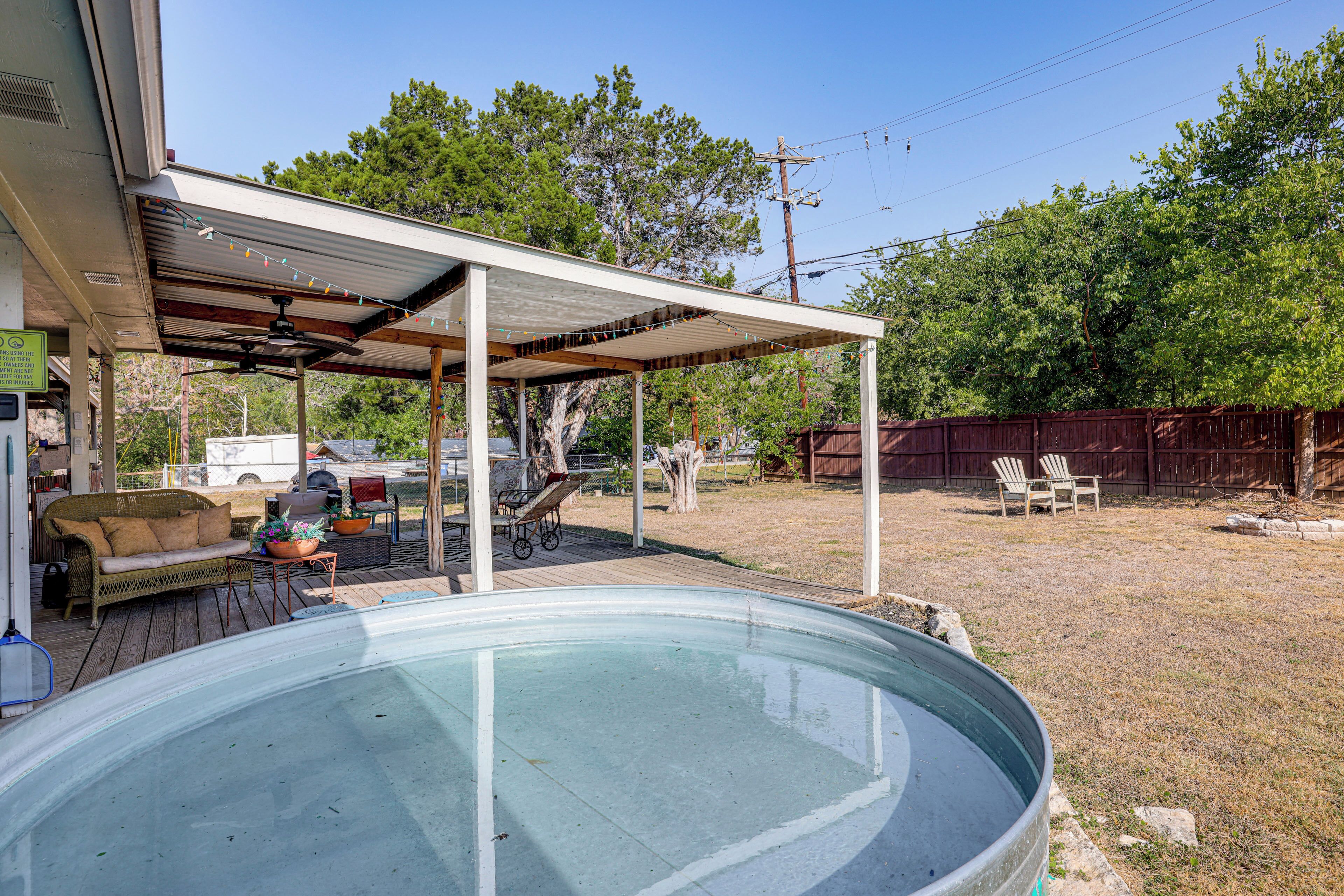 A backyard with a swimming pool, covered patio, and outdoor furniture.