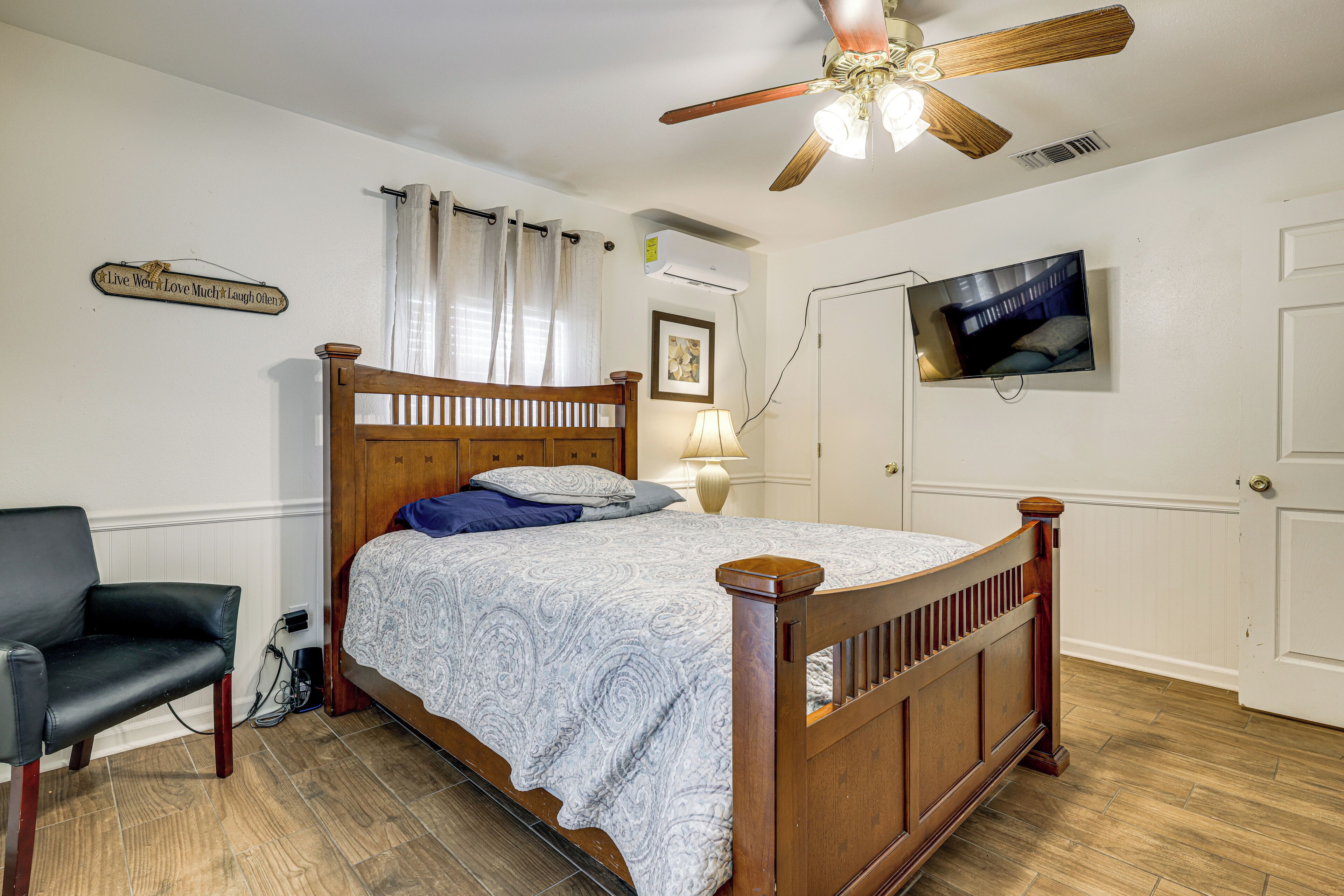 A bedroom with a wooden bed, a chair, a television, and a ceiling fan.