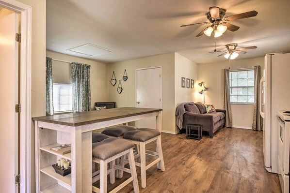 A compact living space with a kitchenette, a dining area with stools, a sofa, and a ceiling fan.