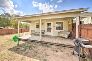 A covered porch with a bench and chairs, a grill, and a wooden fence.