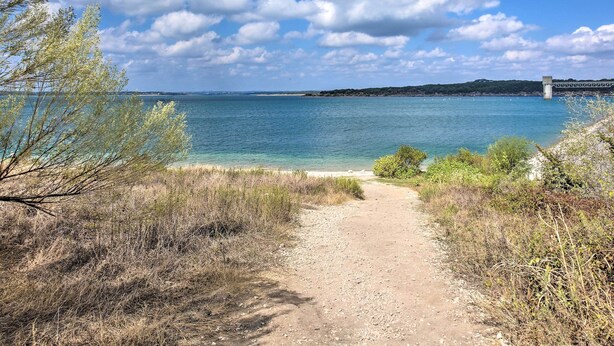 A coastal path leading to a beach with a bridge in the distance. - Cozy Canyon Lake Cottage: 1 Mi to Guadalupe River! (Canyon Lake)