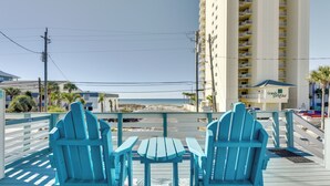 A view from a balcony with two turquoise Adirondack chairs and a small table, overlooking a beach and a tall hotel building. - PCB Apt w/ Balcony & Gulf Views: Walk to Beach (Panama City Beach)