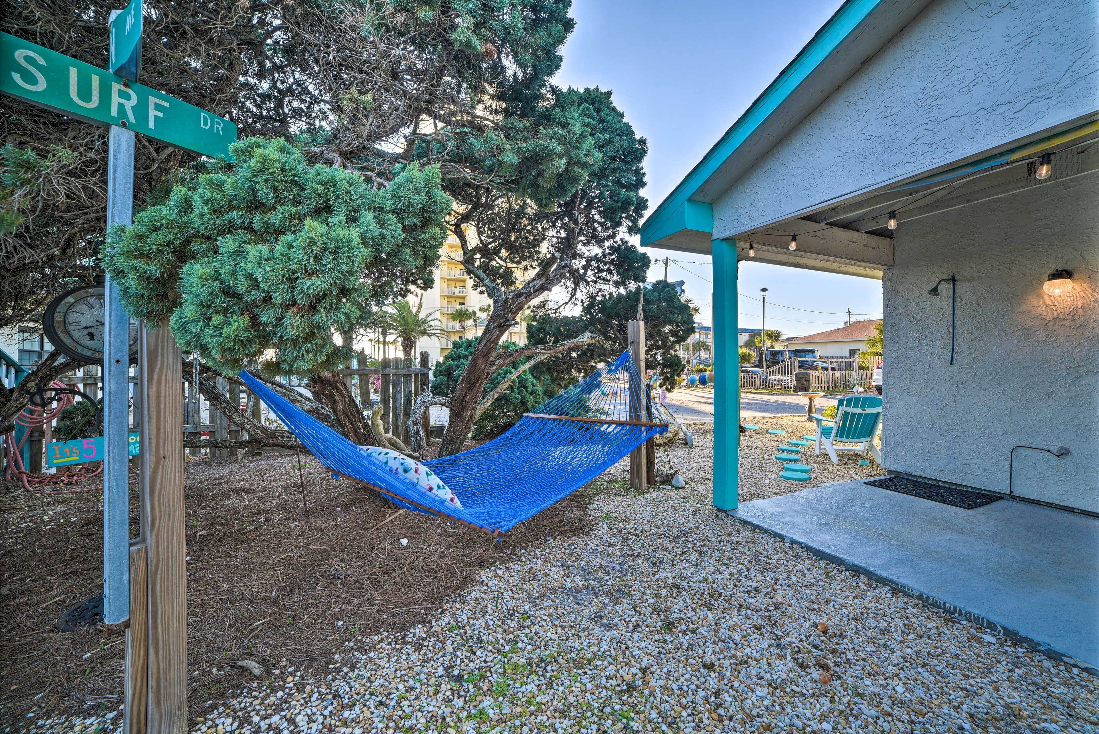 A hammock under a street sign, a building with a porch, and a tree.