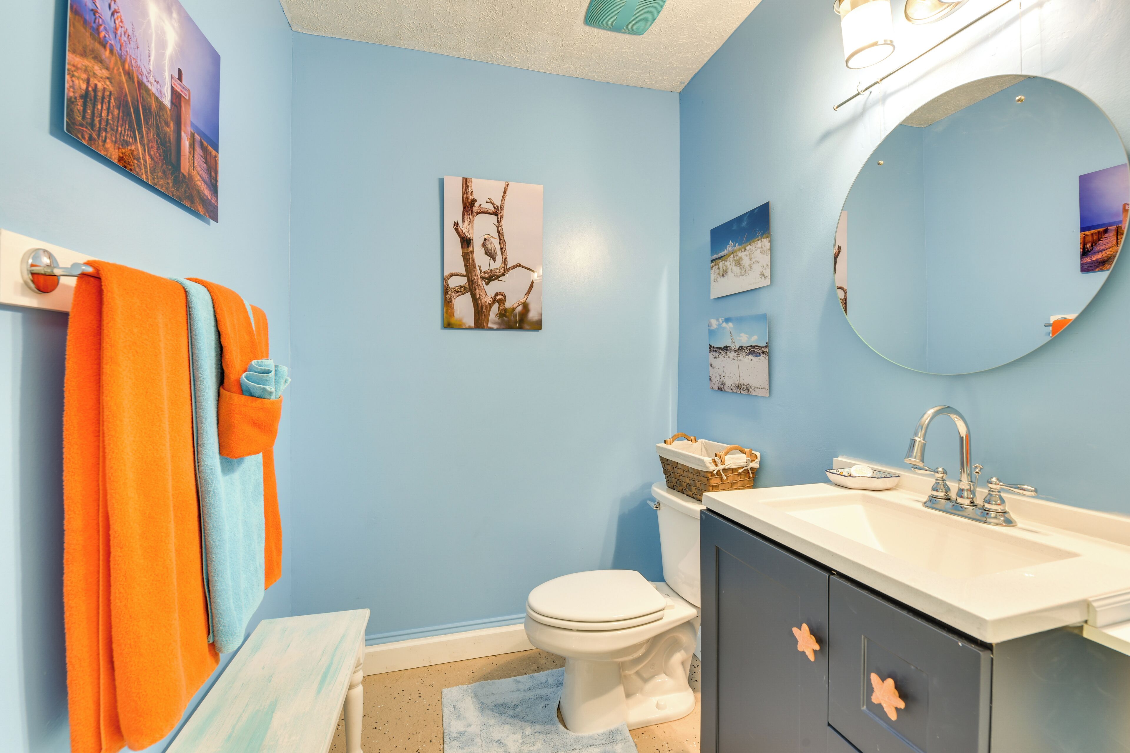 A bathroom with a blue wall, a white toilet, a sink with a mirror, and a towel rack with orange and blue towels.