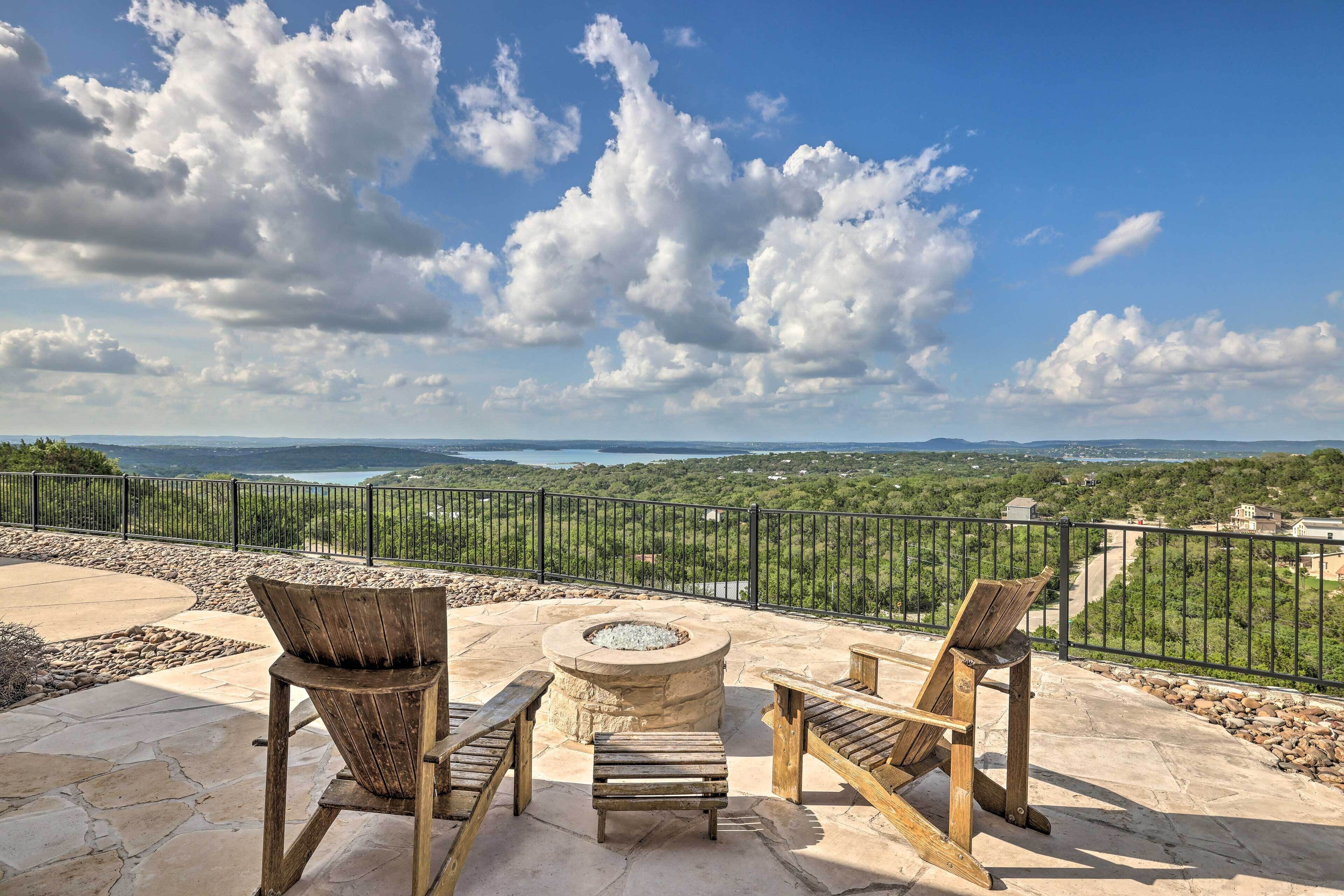An outdoor patio with stone flooring, wooden Adirondack chairs, and a circular stone fire pit.