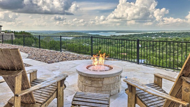 A stone fire pit surrounded by wooden chairs on a patio with a view of a green landscape and a body of water. - Lakeview Escape w/ Hot Tub, 1 Mi to Canyon Lake (Canyon Lake)