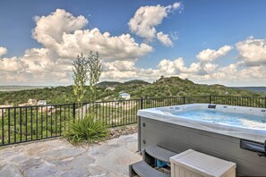 Een hottub op een terras van natuursteen, met uitzicht op heuvels en een hek.