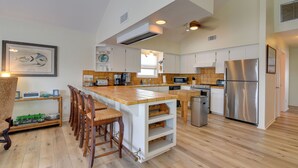 A spacious kitchen with a central island, wooden chairs, a stainless steel refrigerator, and white cabinetry.