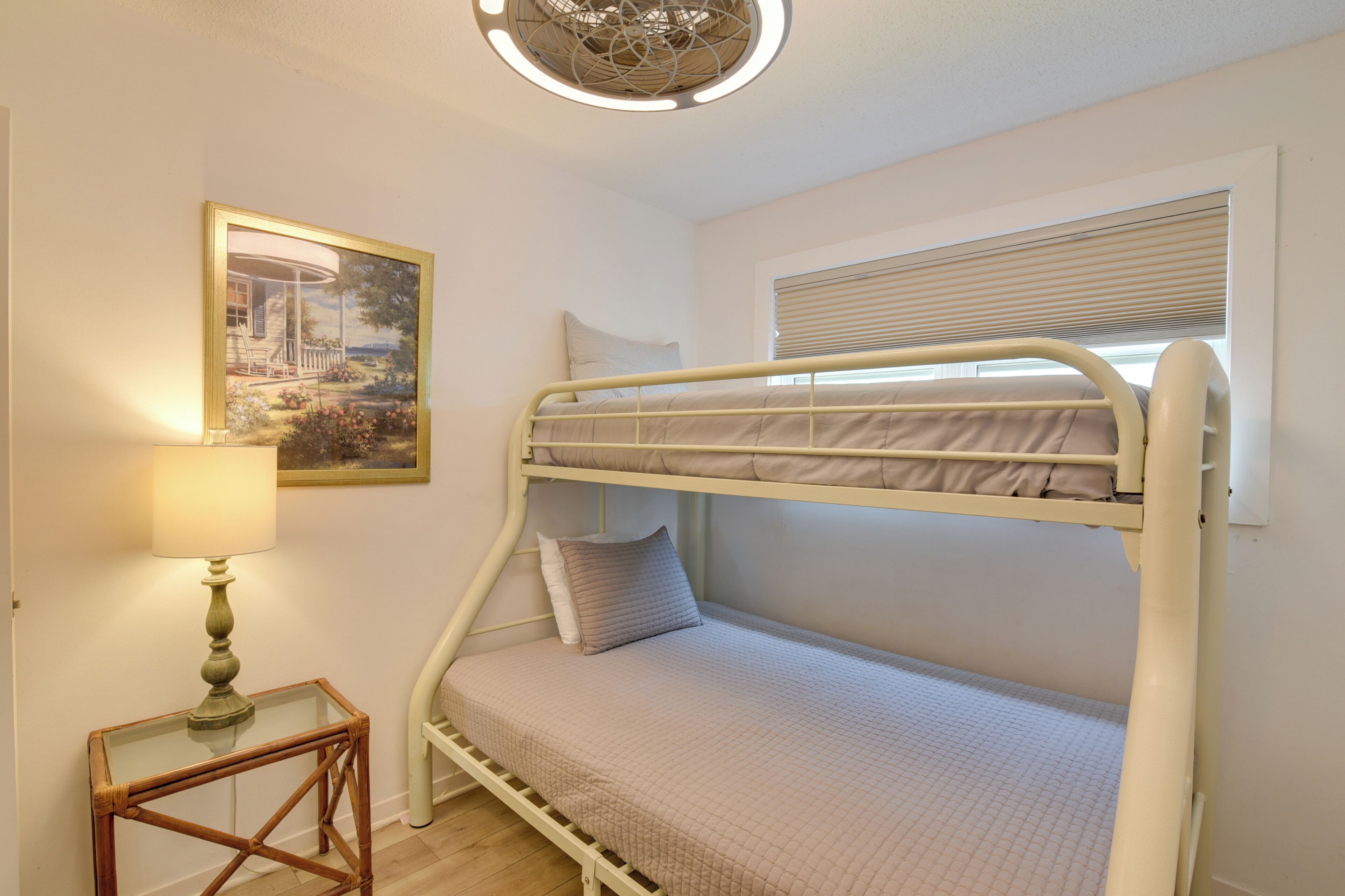 A bunk bed room with a lamp, a framed picture, and a window with blinds.