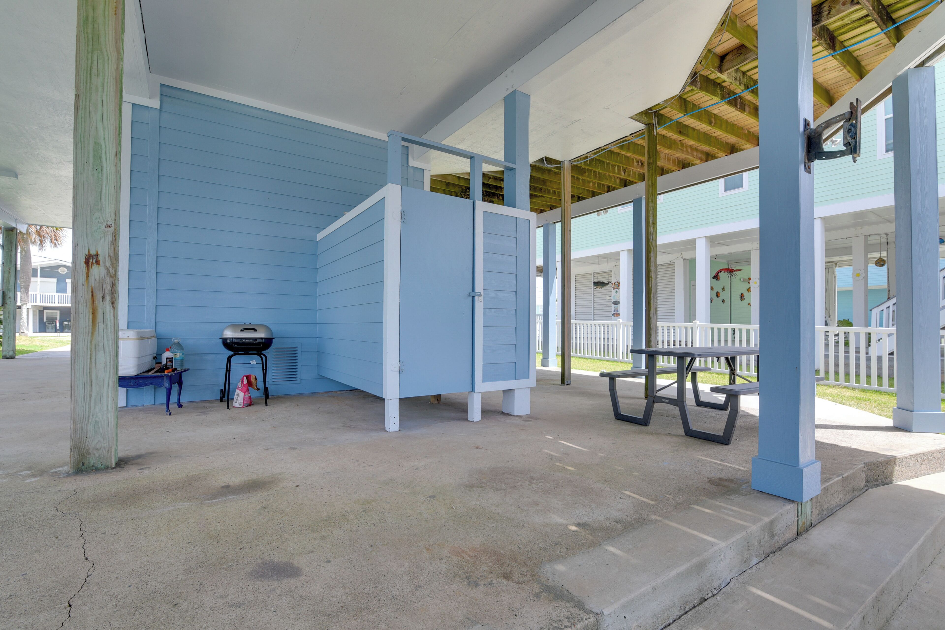 A covered outdoor area with a blue building, a barbecue grill, and a picnic table.
