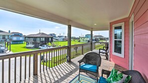 A covered porch with a view of a neighborhood, a wicker chair, and a small table. - Walk to Sea Isle Beach: Bright Galveston Home! (Galveston)