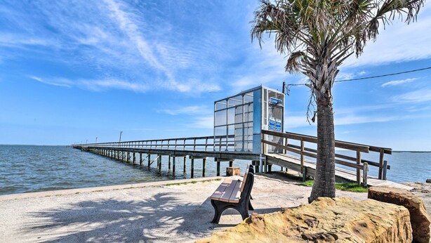 A beach with a wooden pier extending into the water, a bench, and a small structure with a sign. - Walk to Sea Isle Beach: Bright Galveston Home! (Galveston)