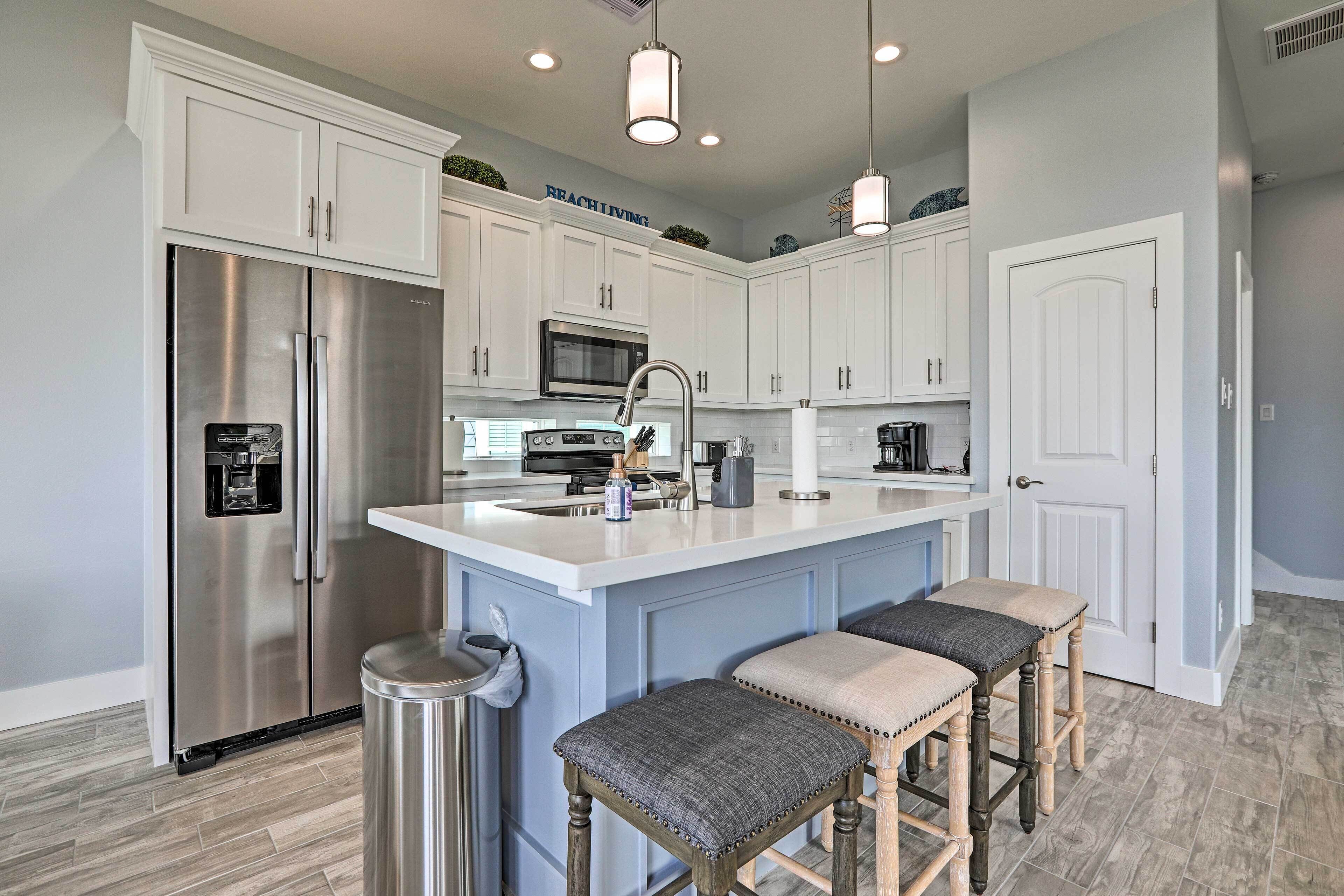 A modern kitchen with white cabinets, stainless steel appliances, a central island with bar stools, and a clean, organized layout.
