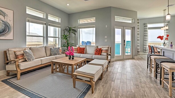 A spacious living room with a sofa, ottomans, a coffee table, and a dining area with bar stools. - Villa Azul Galveston Home: Modern & Beachfront! (Galveston)