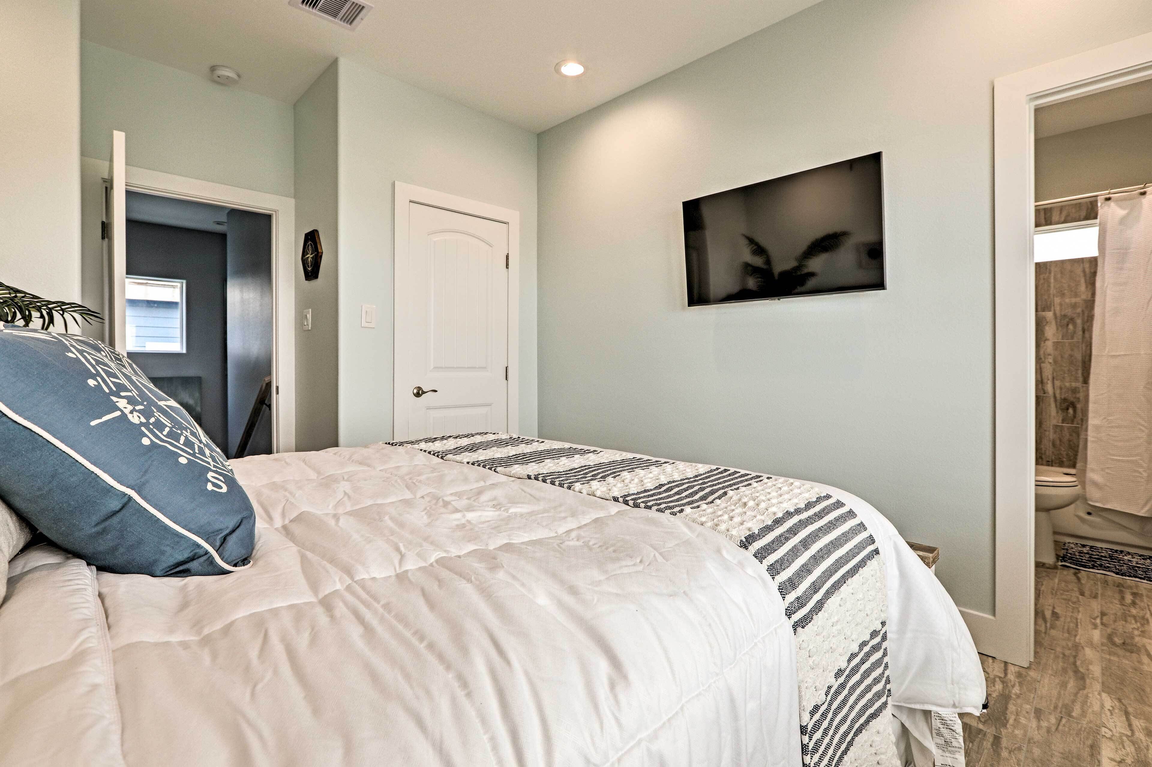 A bedroom with a bed, a door, a framed picture on the wall, and a bathroom visible through an open door.