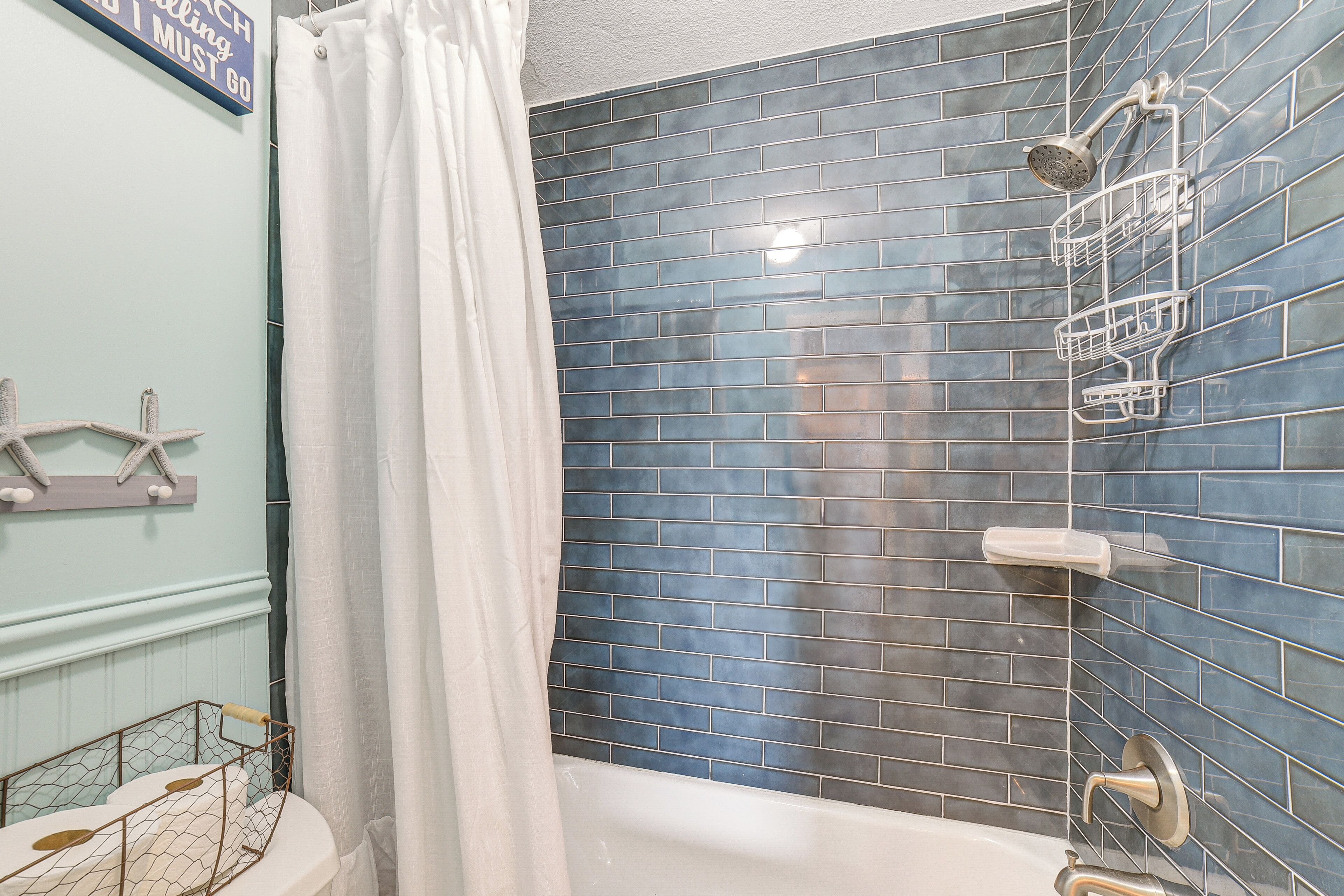 A bathroom with a bathtub, a shower, and a blue-tiled wall.