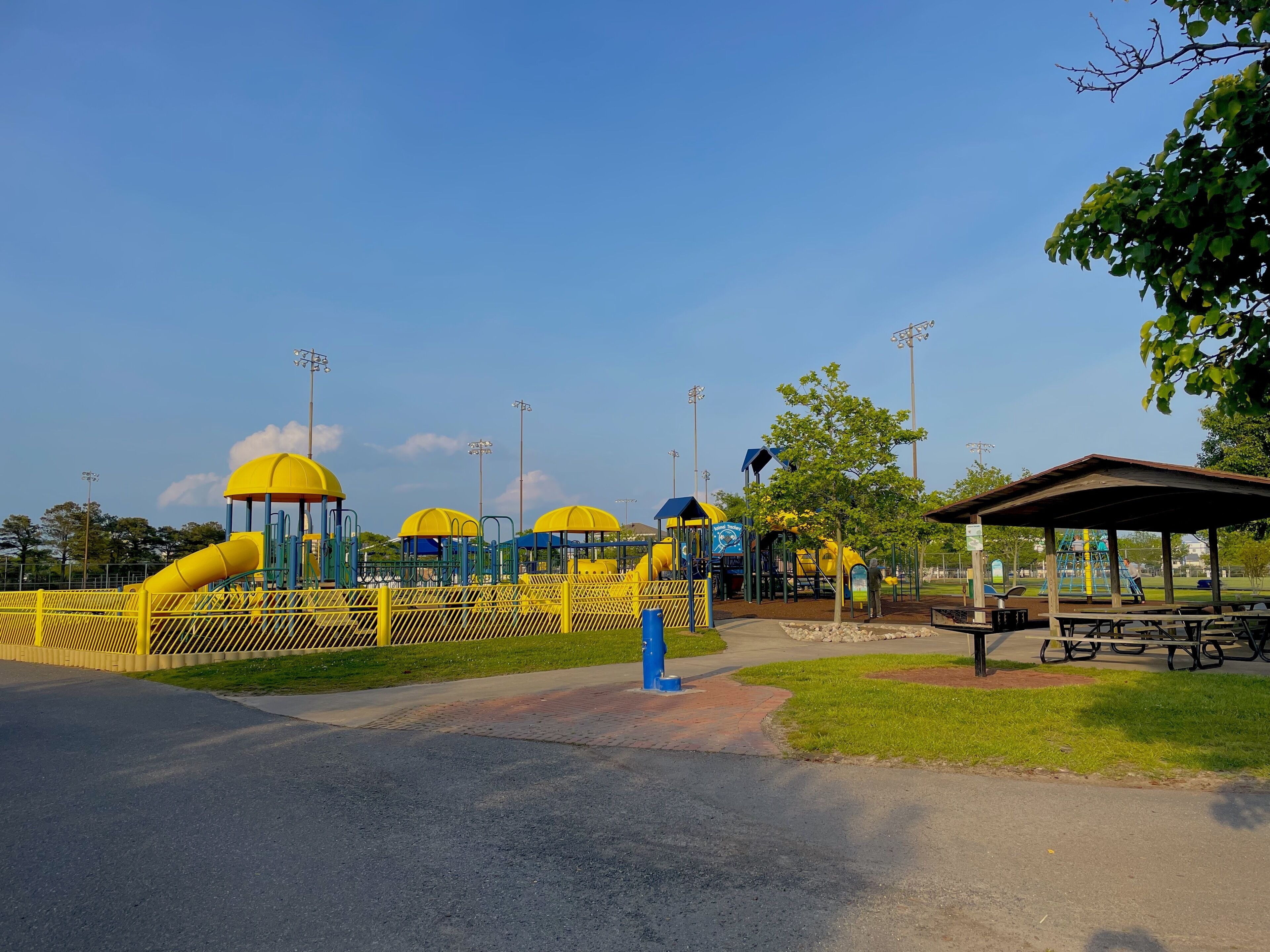 Un parque infantil con estructuras de juego amarillas y azules, una zona de estar cubierta y una mesa de picnic.