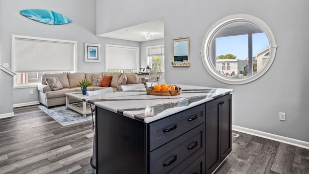 Een moderne woonkamer met een groot raam, een ronde spiegel en een keukeneiland met een marmeren aanrecht.