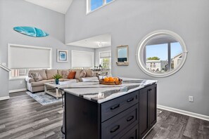 A modern living room with a large window, a round mirror, and a kitchen island with a marble countertop.