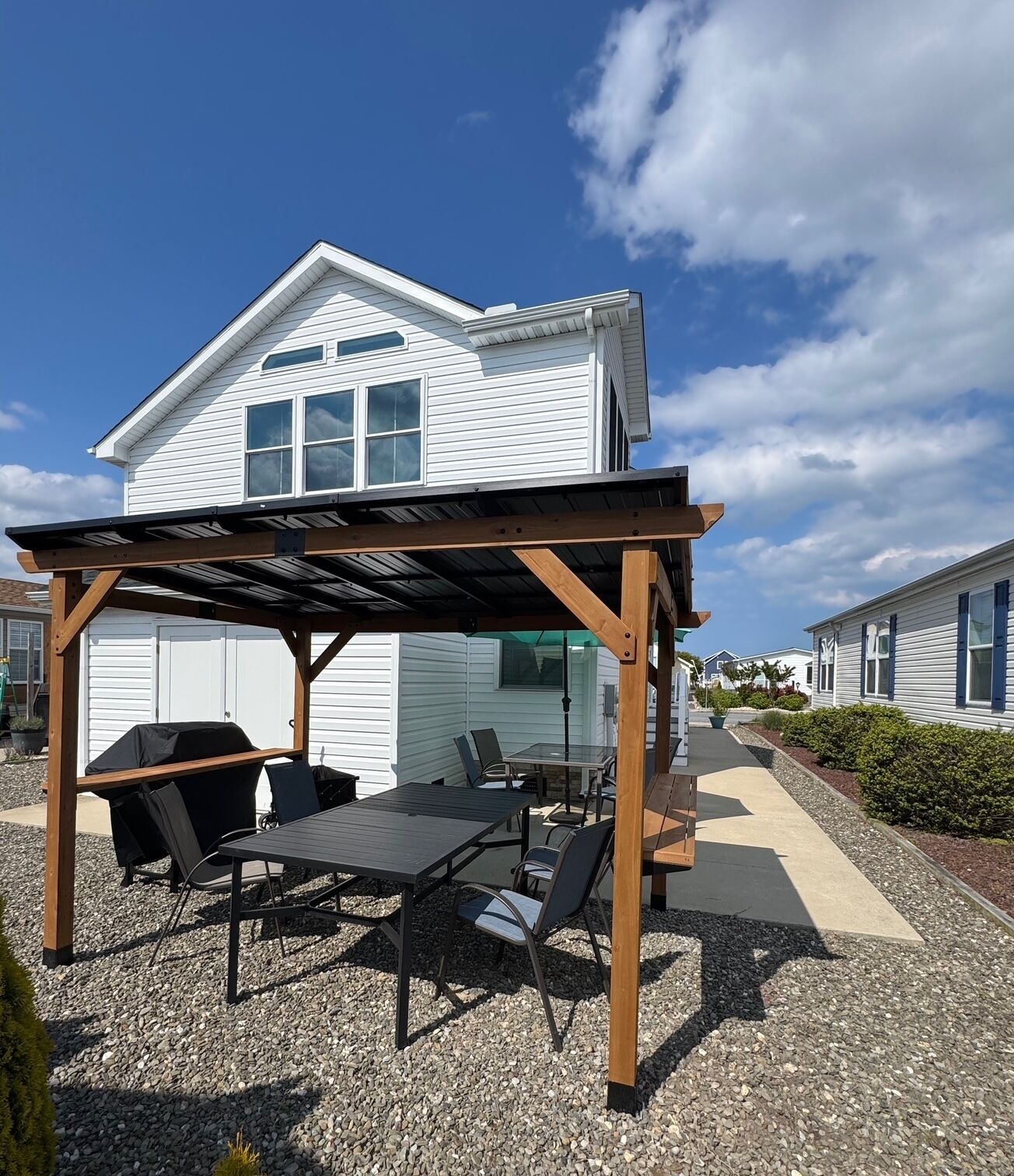 A covered patio with outdoor furniture, a grill, and a house in the background.