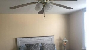 Ein Schlafzimmer mit einem Bett, einem Nachttisch, einer Lampe und einem Deckenventilator.