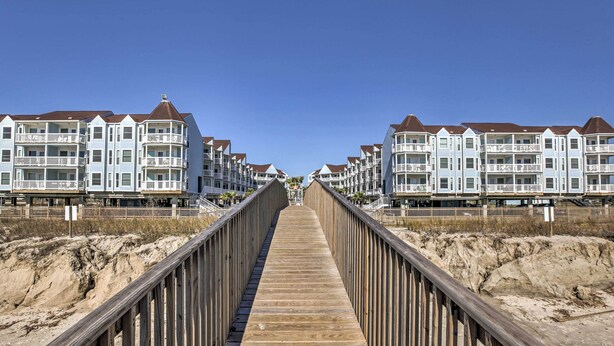 Une promenade en bois mène à une série de copropriétés situées en bord de mer, toutes dotées de balcons.