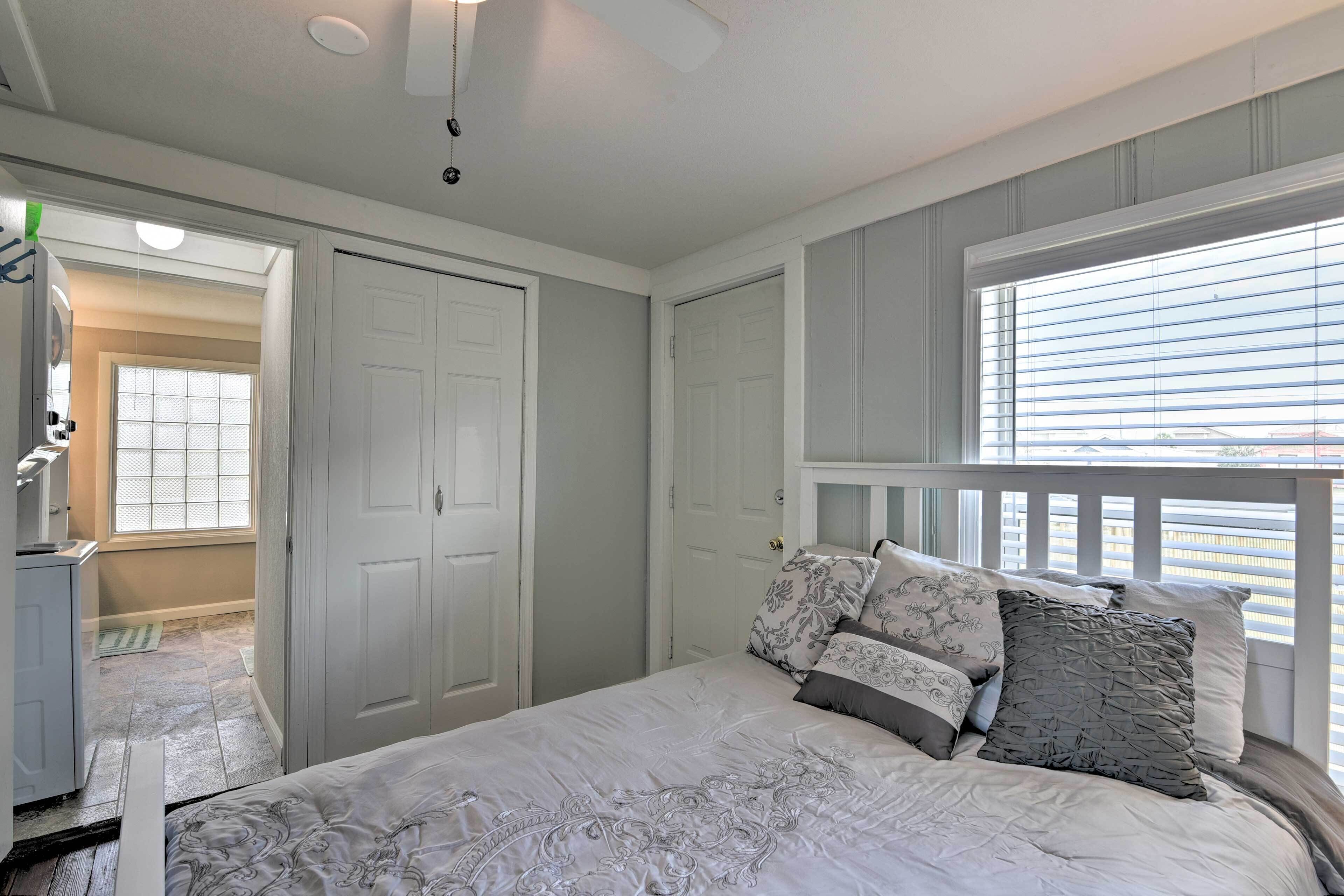 A bedroom with a bed, a dresser, a door, and a window with blinds.