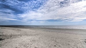 A beach with a wide sandy shore and a clear view of the ocean under a partly cloudy sky.