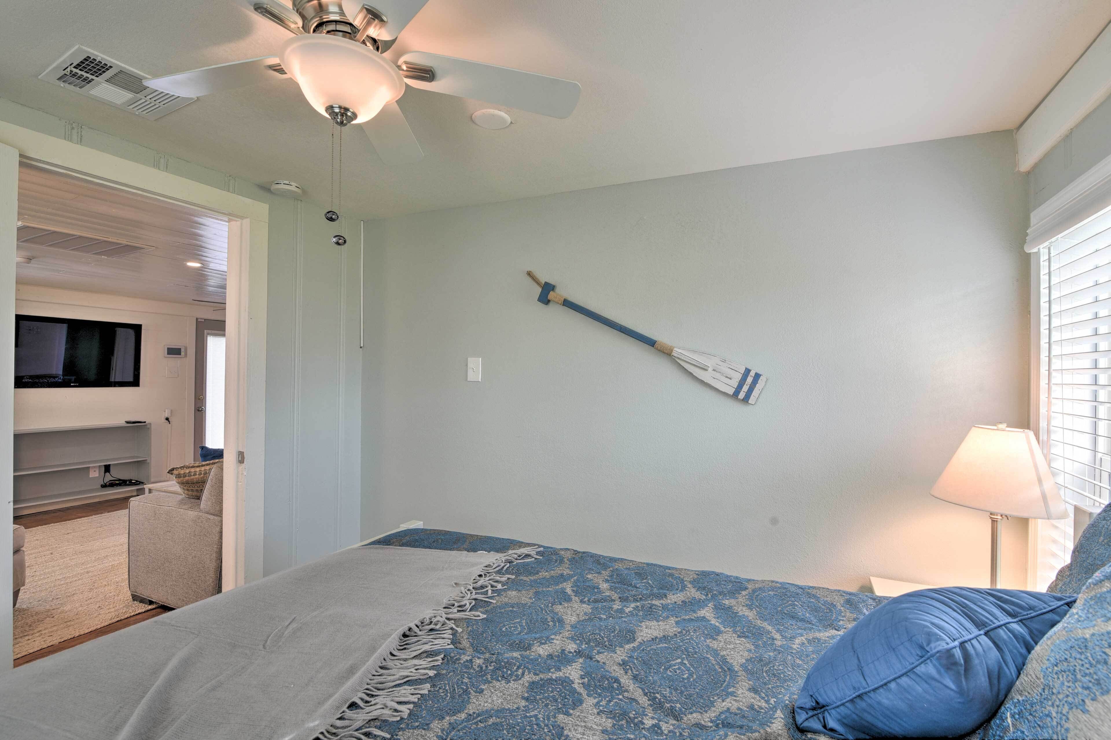 A bedroom with a bed, a ceiling fan, a wall-mounted TV, and a window with blinds.