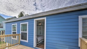 A blue house with a wooden deck, a bedroom with a bed, and a bathroom with a shower.