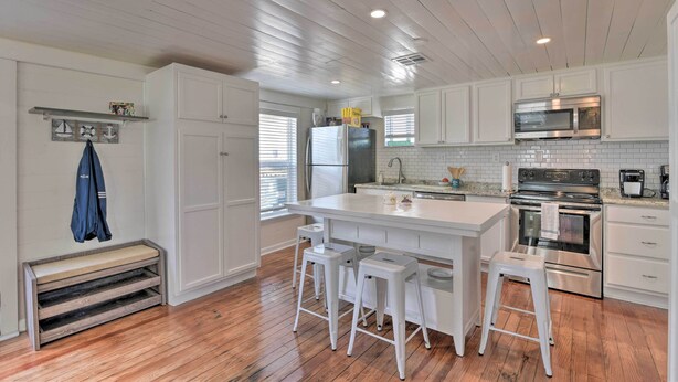 A modern kitchen with white cabinetry, a central island with stools, stainless steel appliances, and a wooden floor.