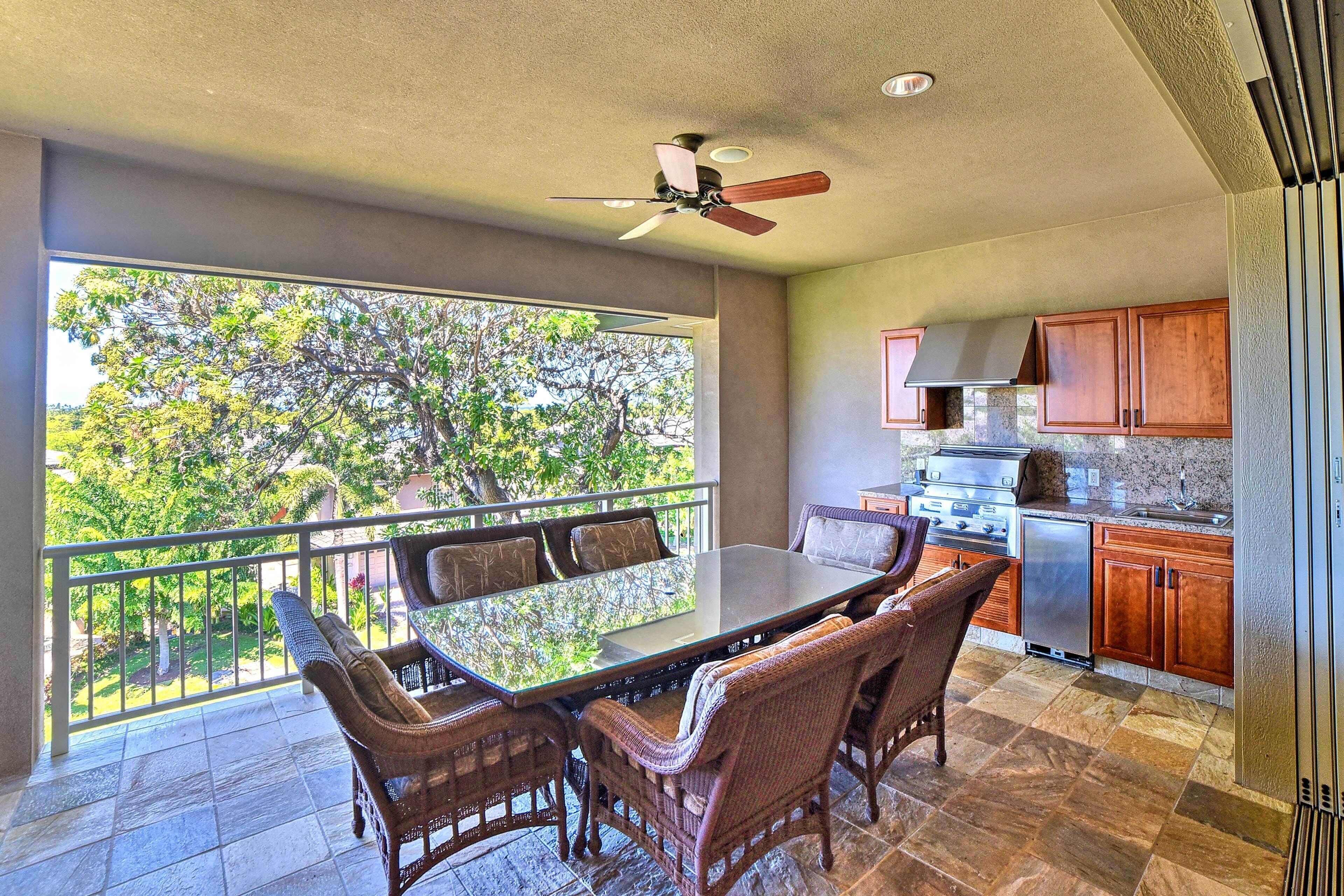 A balcony with wicker furniture, a glass table, and a ceiling fan.