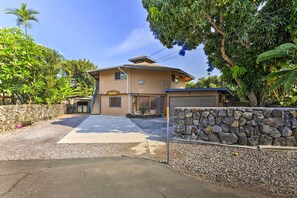 A two-story house with a stone wall and a paved driveway leading to the garage. - Kailua-kona Home w/ Tropical Bar: Walk to Beach! (Kailua-Kona)