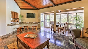 A spacious living area with a wooden ceiling, a kitchen with a granite countertop, and a dining area with natural light from large windows.